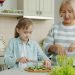 Grandma and cute child are cooking salad for lunch talking making healthy meal at home. Domestic activities, family life and happy childhood concept.