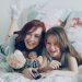 Laughing happy mother and cute daughter watching funny cartoon movie on TV while lying on bed at home in morning have fun at cozy bedroom